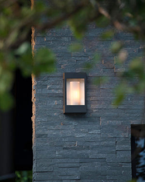 Outdoor wall light fixture on a stone wall with blurred greenery in the foreground