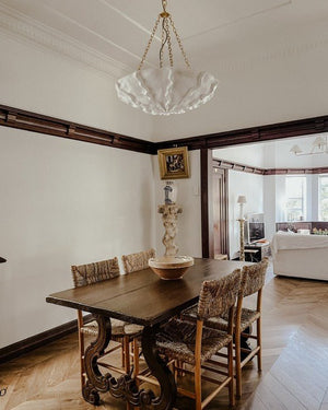 Dining room with wooden table and chairs, plaster chandelier, and view of living room.
