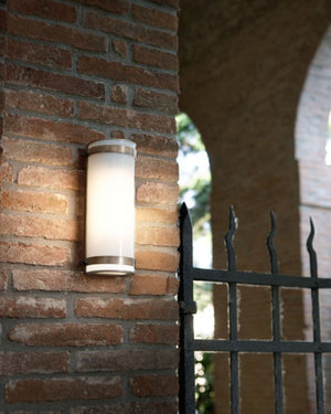 Outdoor wall light fixture on a brick wall with a gated entrance in the background