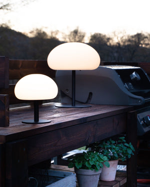 Two sizes of the outdoor lamps on a wooden surface with a scenic background