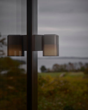 Wall light with perforated shade in anthracite finish on facade with ocean in background