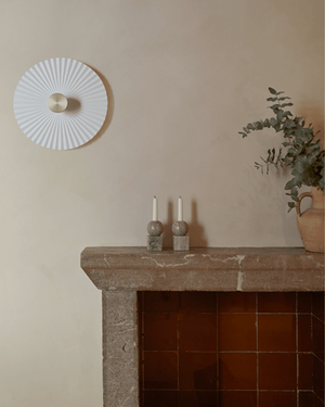 Decorative wall light fixture above a stone fireplace with candles and a plant.