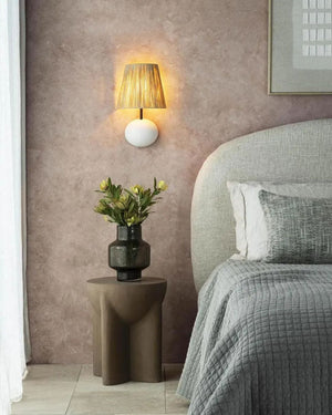 Raffia shade wall light with white resin backplate installed above bedside table