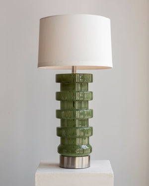 Green glass table lamp with a white shade on a neutral background