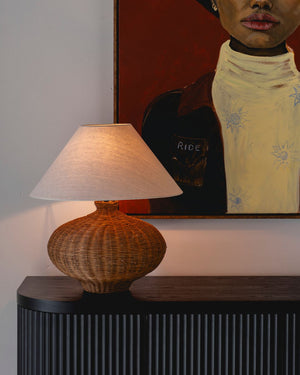 Wicker table lamp on black counter in front of painting