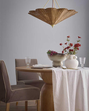 A scalloped rattan pendant lighting hanging above a wooden table with white cloth in a modern dining interior