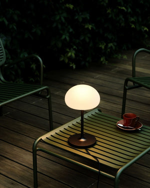 Portable Table lamp on a green table with a cup and saucer in a dark outdoor setting - Lighting Collective 