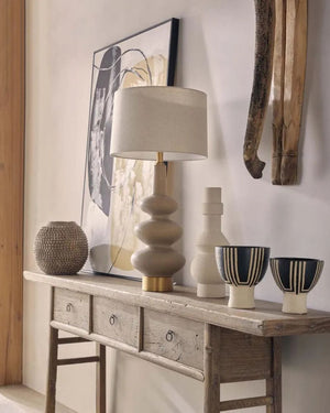 Decorative table with lamp, vases, and bowls against a wall with abstract art.