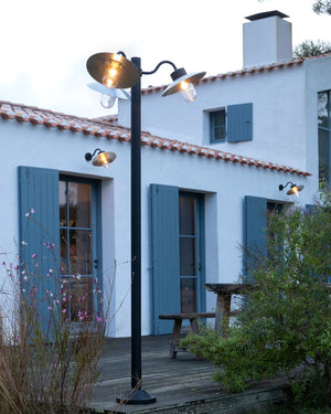 Outdoor lamp post with three lights in front of a white house with blue shutters.