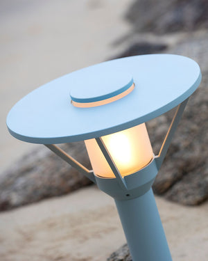 Blue outdoor lamp on a beach with rocks in the background