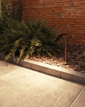 Outdoor setting with a brick wall, green bush, and Solid Cast Brass Hydra Spike Light 