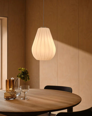 Pleated opal pendant lit above round dining table with amber glassware in warm Scandinavian interior