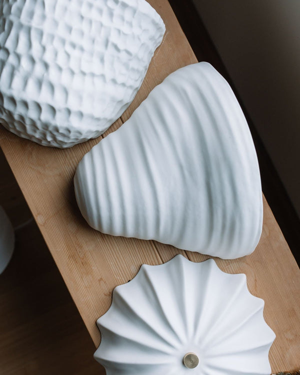 Three white textured ceramic wall lamps displayed on bench