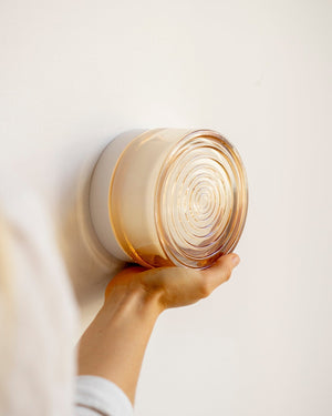 A hand holding a round, rippled, transparent amber-coloured glass wall light