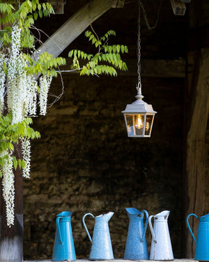Vintage-style lantern hanging above a row of colorful jugs against a rustic stone wall.