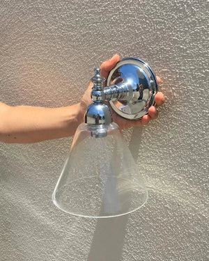 Person holding a chrome outdoor light fixture against a textured wall.