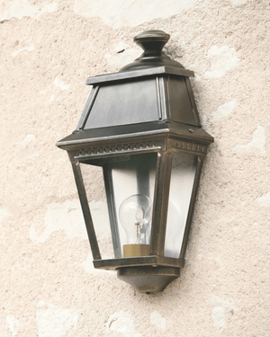 A classic french outdoor wall lantern light fixture with clear glass panels, mounted on a textured wall