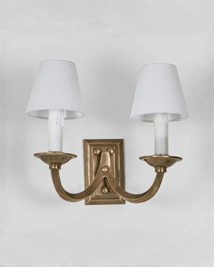Brass wall sconce with two white lampshades on a light gray background