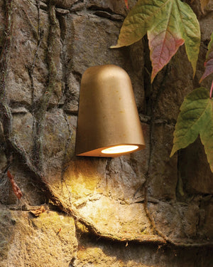 Brass outdoor wall light fixture on a stone wall with leaves in the background