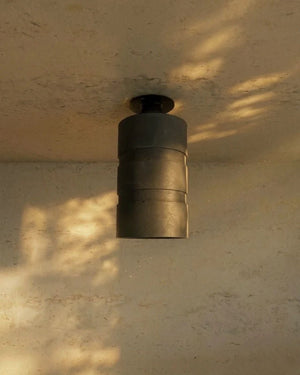 Tubular Concrete Downlight in charcoal mounted on ceiling with dappled golden light across textured plaster walls