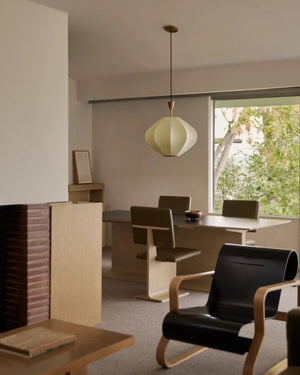 A modern interior room scene with a webbed fibre lantern pendant hanging above , dining table, chairs, and a black armchair in a living room