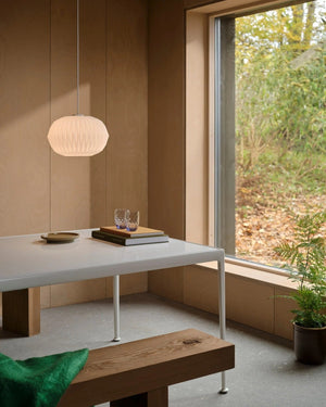 Wide pleated glass pendant lit above white dining table in warm timber-lined Scandinavian interior